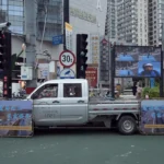 A truck driving down a street next to tall buildings
